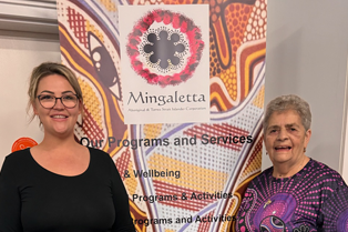 Chloe and Aunty Di standing in front of a Mingaletta banner