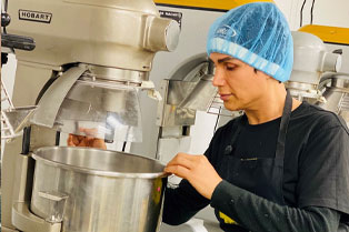 Javid, wearing a hairnet and looking into a large mixing bowl