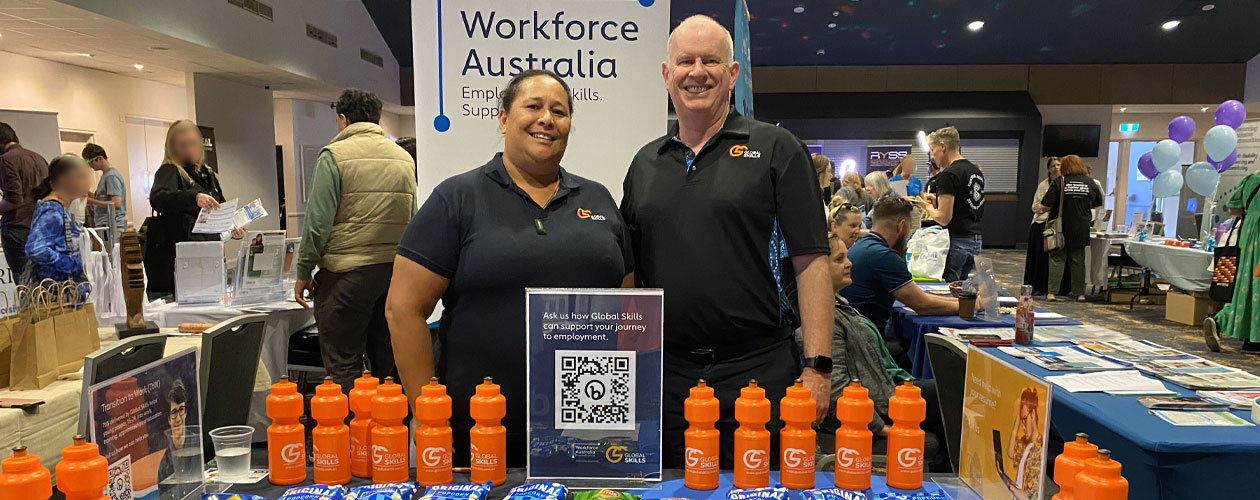 Global Skills staff, Jennifer and Simon, at our Future Choices Expo stand behind a table displaying branded merchandise and flyers, showcasing our services.