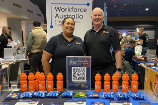 Global Skills staff, Jennifer and Simon, at our Future Choices Expo stand behind a table displaying branded merchandise and flyers, showcasing our services.