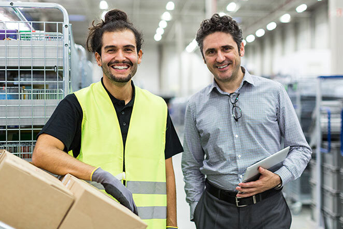 2 men in warehouse setting. One in high vis vest the other in dress shirt