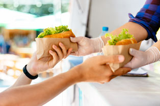 Hands from a food truck window passing salad rolls to another set of hands