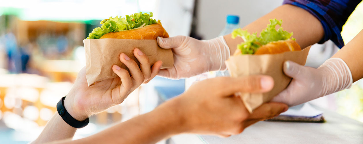 Hands from a food truck window passing salad rolls to another set of hands