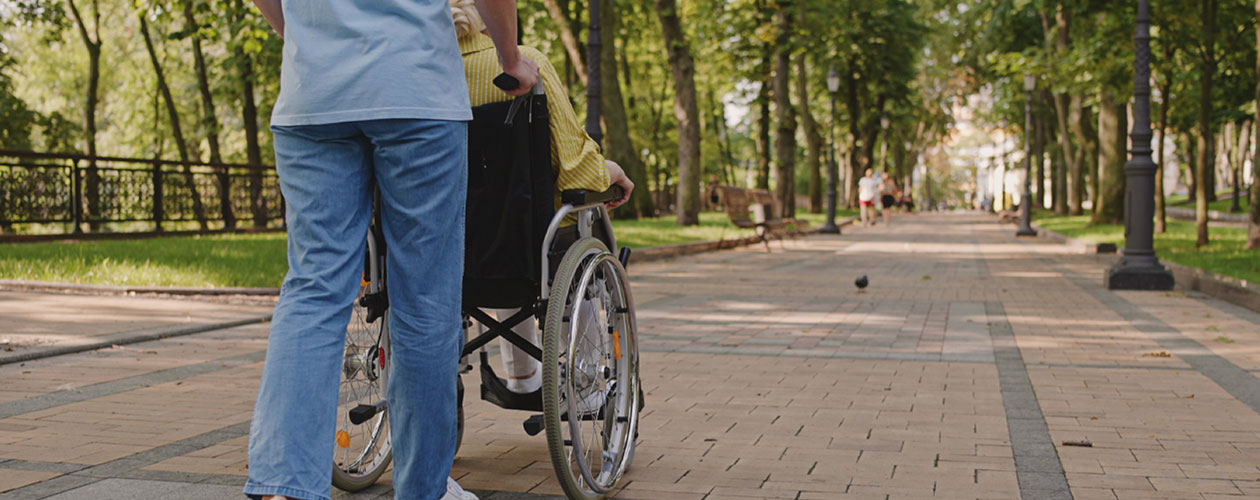 Support person pushing a person in a wheelchair along an outdoor path