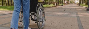 Support person pushing a person in a wheelchair along an outdoor path