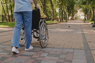 Support person pushing a person in a wheelchair along an outdoor path