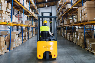 A forklift operator navigates a warehouse aisle, with high shelves stacked with boxes on both sides