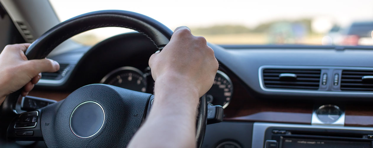 Hands holding the steering wheel of a car, view from the inside of the cabin.